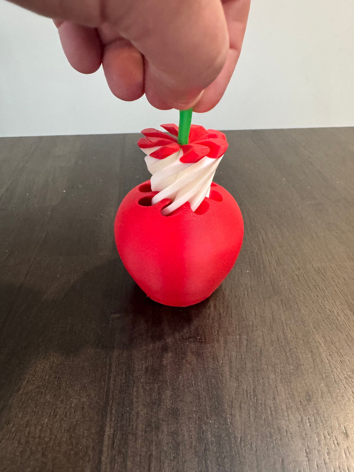 Apple Pass-Through Fidget — a hand drawing the green stem upward to extend the white spiral out of the red apple body.