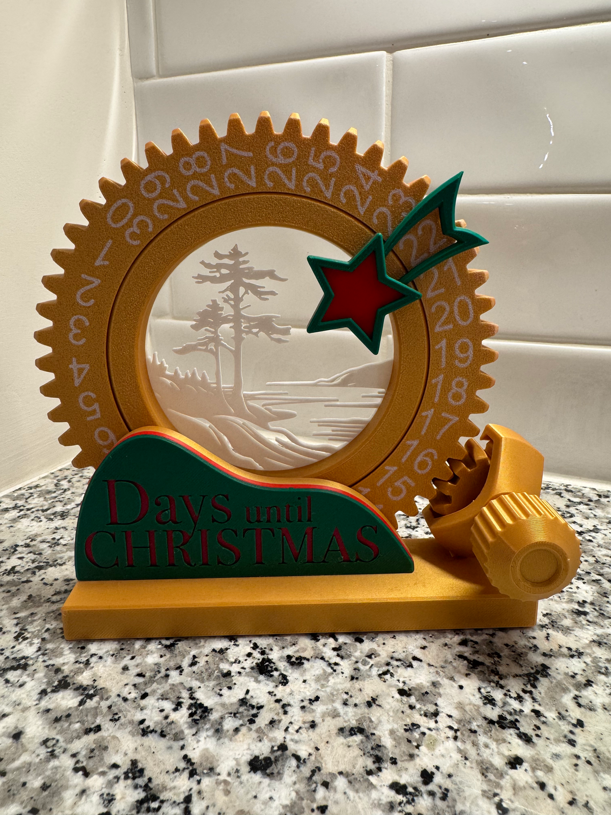 Days Until Christmas Countdown Sign — a gold geared dial numbered around the rim, with a forest scene window, a red and green shooting star, and a green base reading 'Days until CHRISTMAS'.