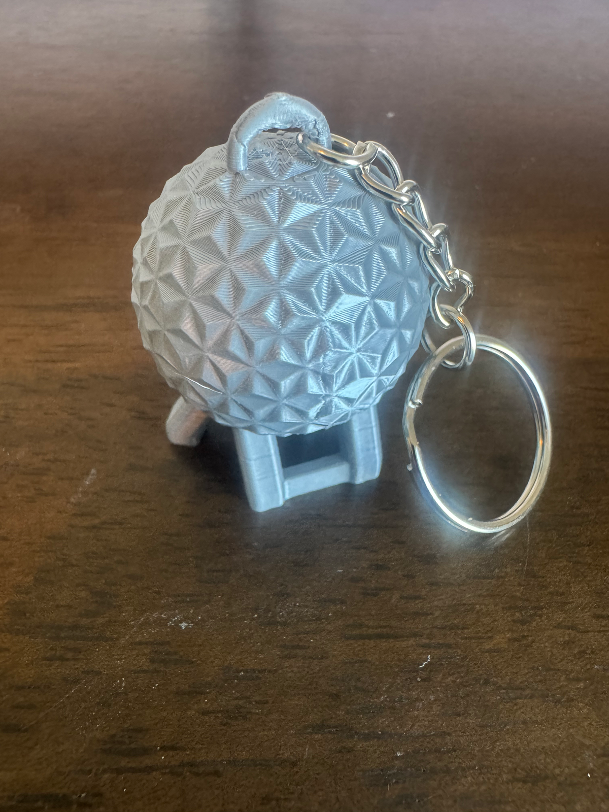 Geodesic Sphere Keychain — a pale blue faceted geodesic sphere on a small stand, attached to a silver keyring, on a wood table.