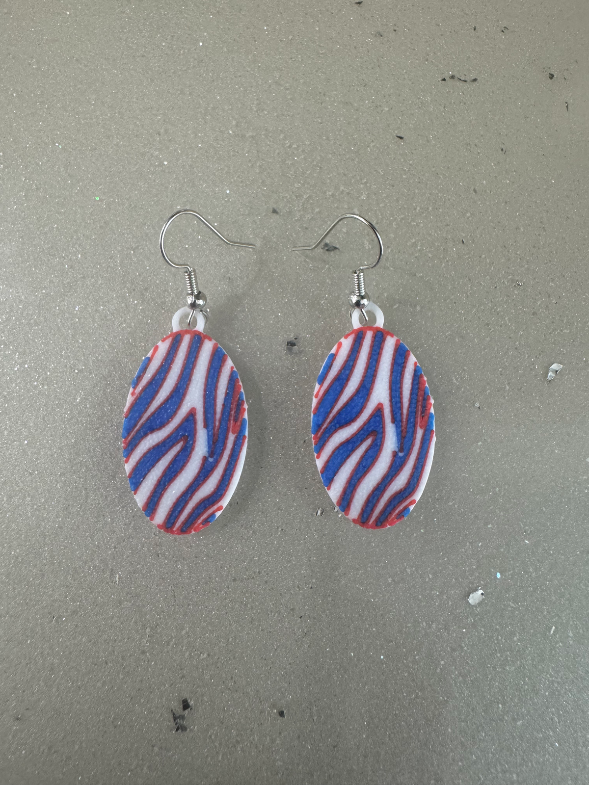 Zigzag Stripe Earrings — a pair of oval dangle earrings with a red, white and blue zigzag stripe pattern on silver hooks.