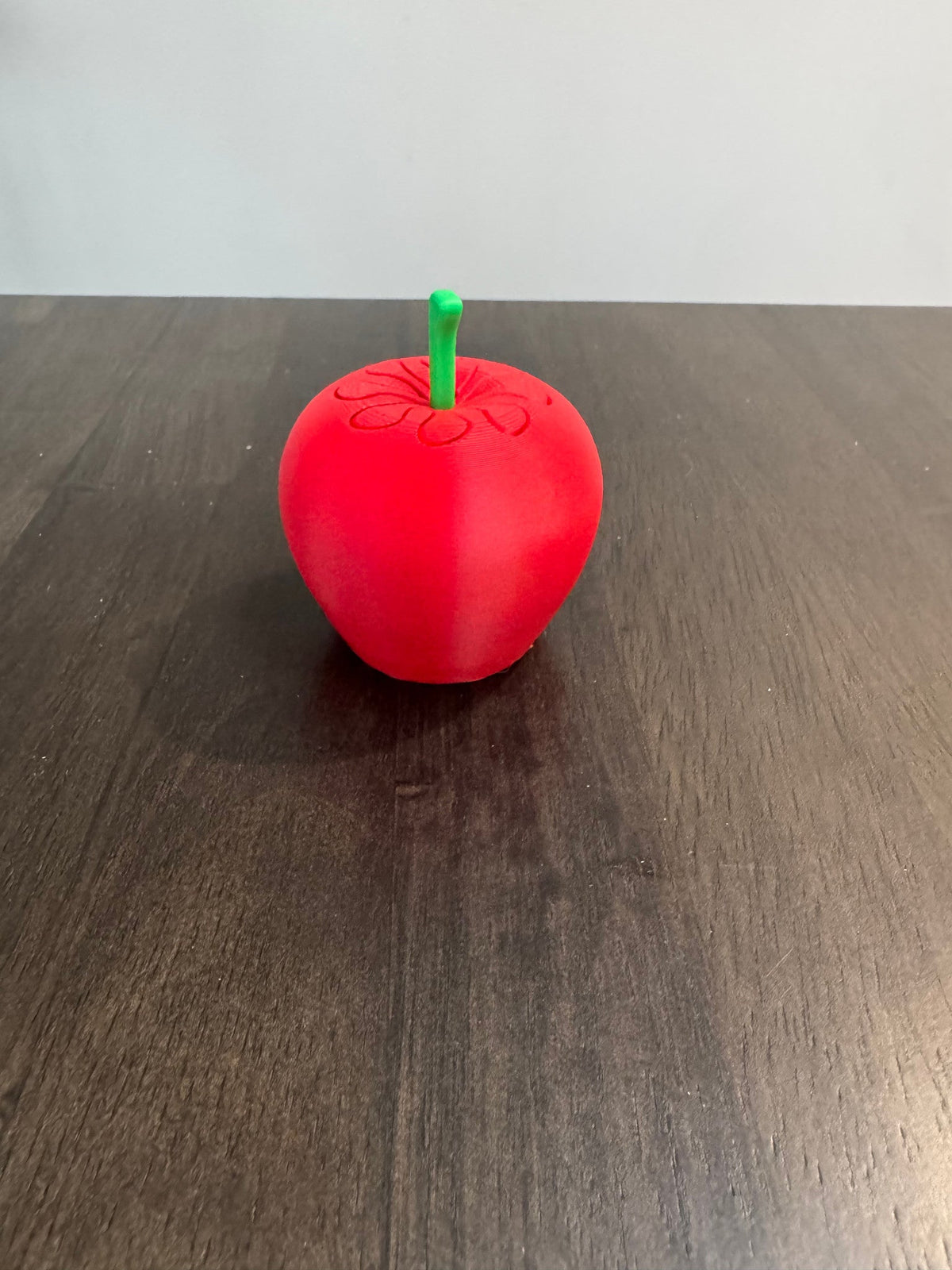 Apple Pass-Through Fidget — the closed red apple-shaped fidget with a green stem, on a dark wood table.