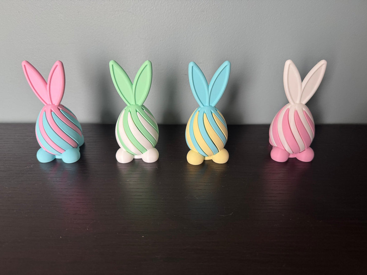 Bunny Egg Spiral Fidgets — Set of 4 — four pastel bunny-shaped spiral fidgets in pink, mint, blue and cream, standing in a row on a dark wood table.