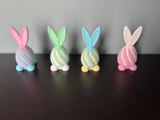 Bunny Egg Spiral Fidgets — Set of 4 — four pastel bunny-shaped spiral fidgets in pink, mint, blue and cream, standing in a row on a dark wood table.