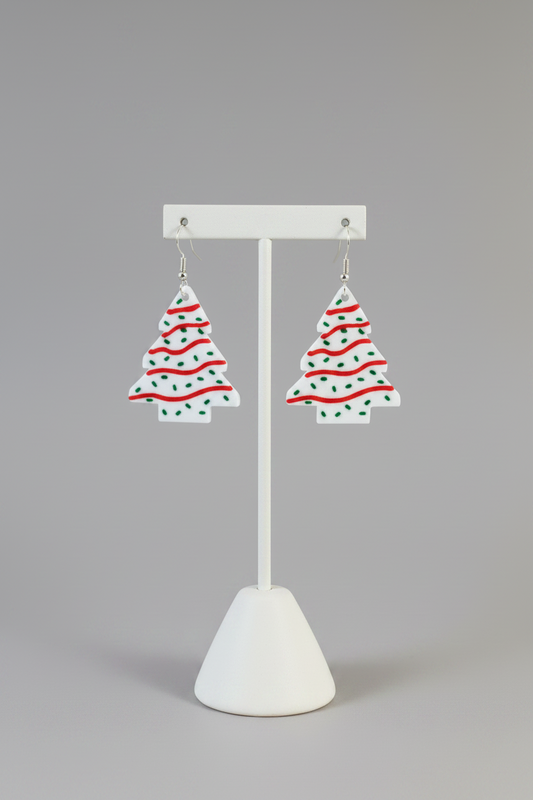 Christmas Tree Snack Cake Earrings — a pair of Christmas tree-shaped dangling earrings with a white base, red wavy stripes, and green dots, on a soft light-gray studio background.