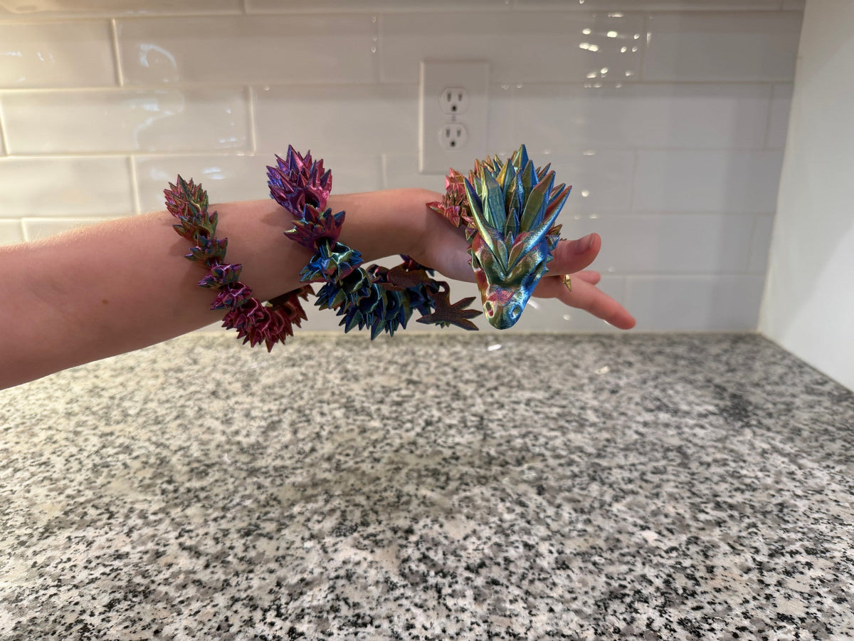 Crystal Dragon — an iridescent purple and green articulated dragon draped over a hand, its head resting on the fingers.