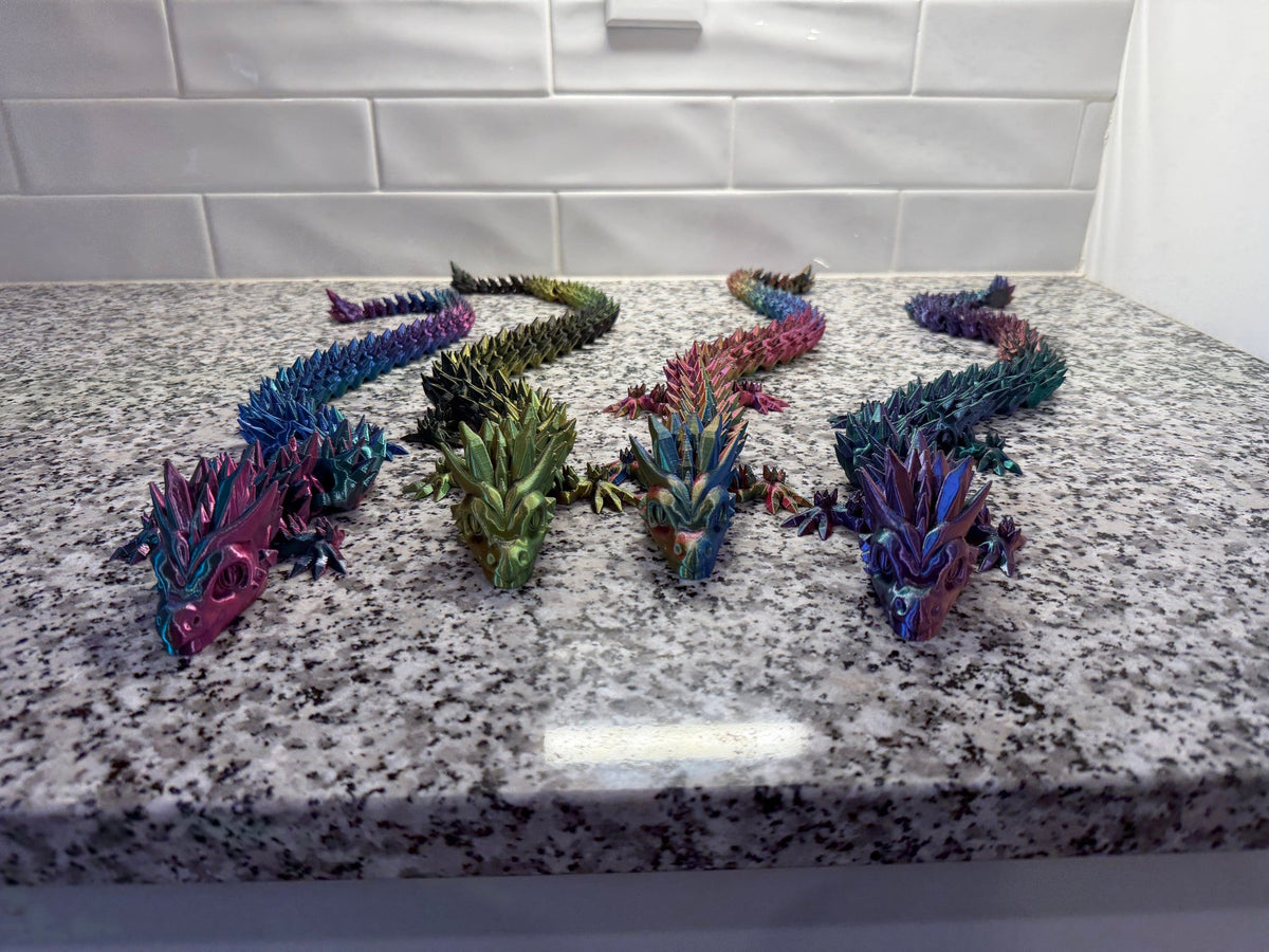 Crystal Dragon — five articulated dragons in blue, pink, green and purple arranged on a granite counter.