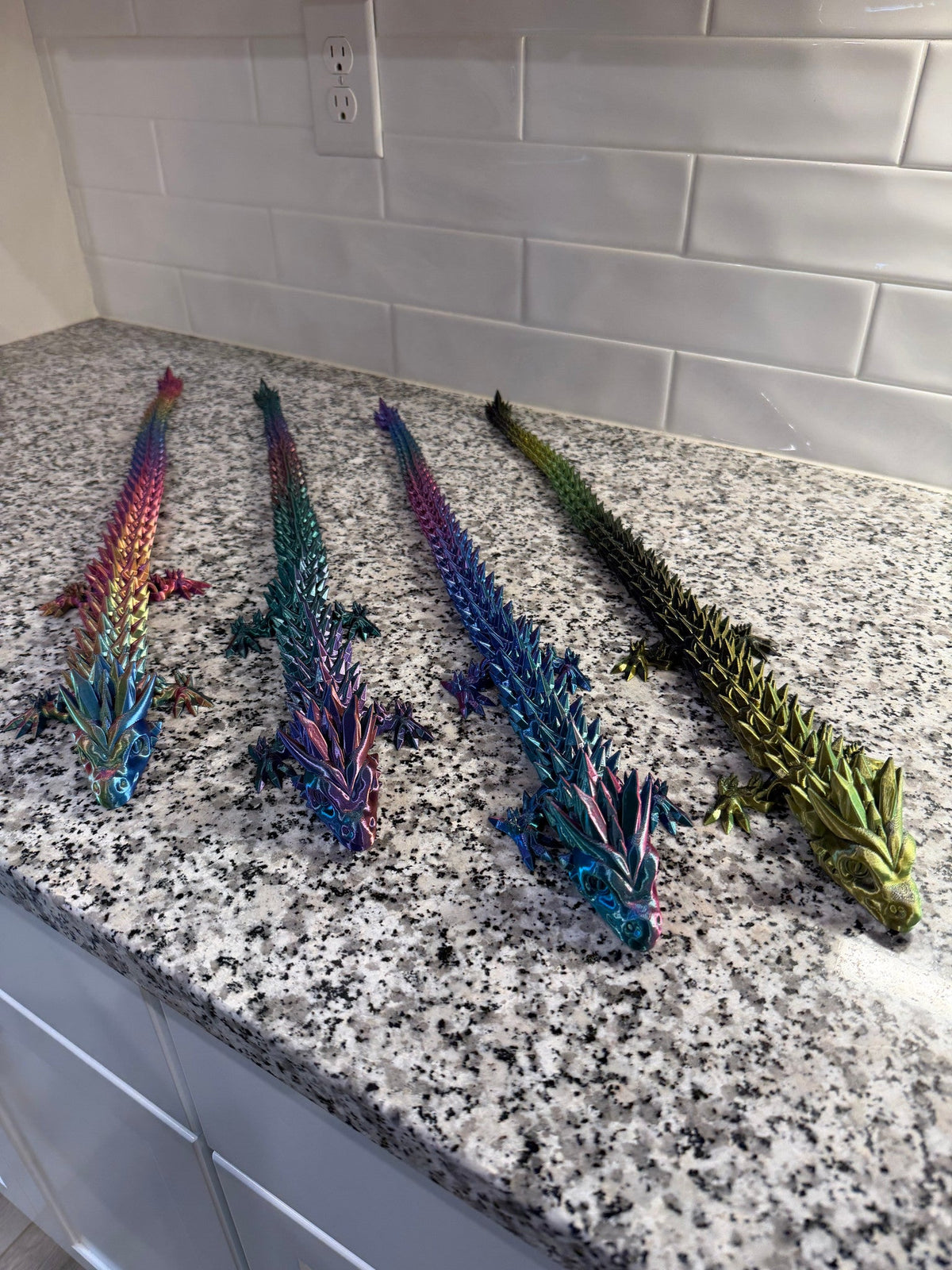 Crystal Dragon — four dragons in pink, blue, purple and olive lined up in a row along the counter edge.