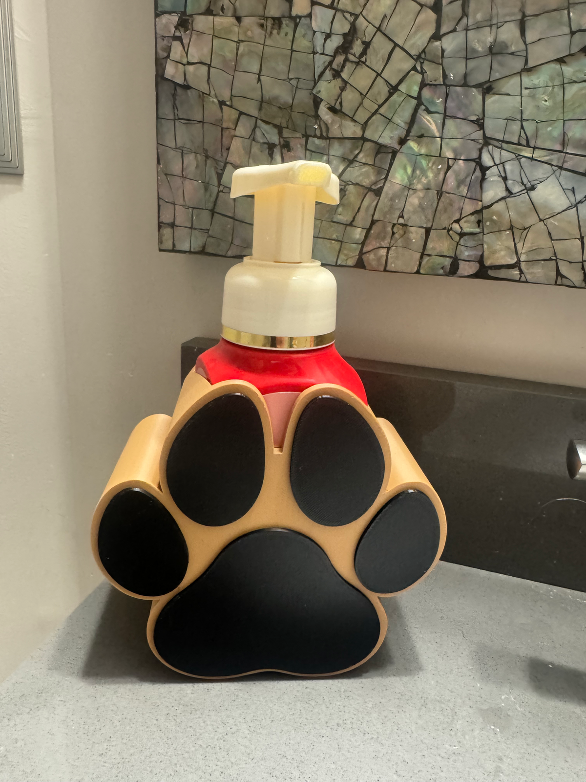 Dog Paw Soap Dispenser Holder — a tan and black paw-print holder cradling a red soap bottle with a cream pump.