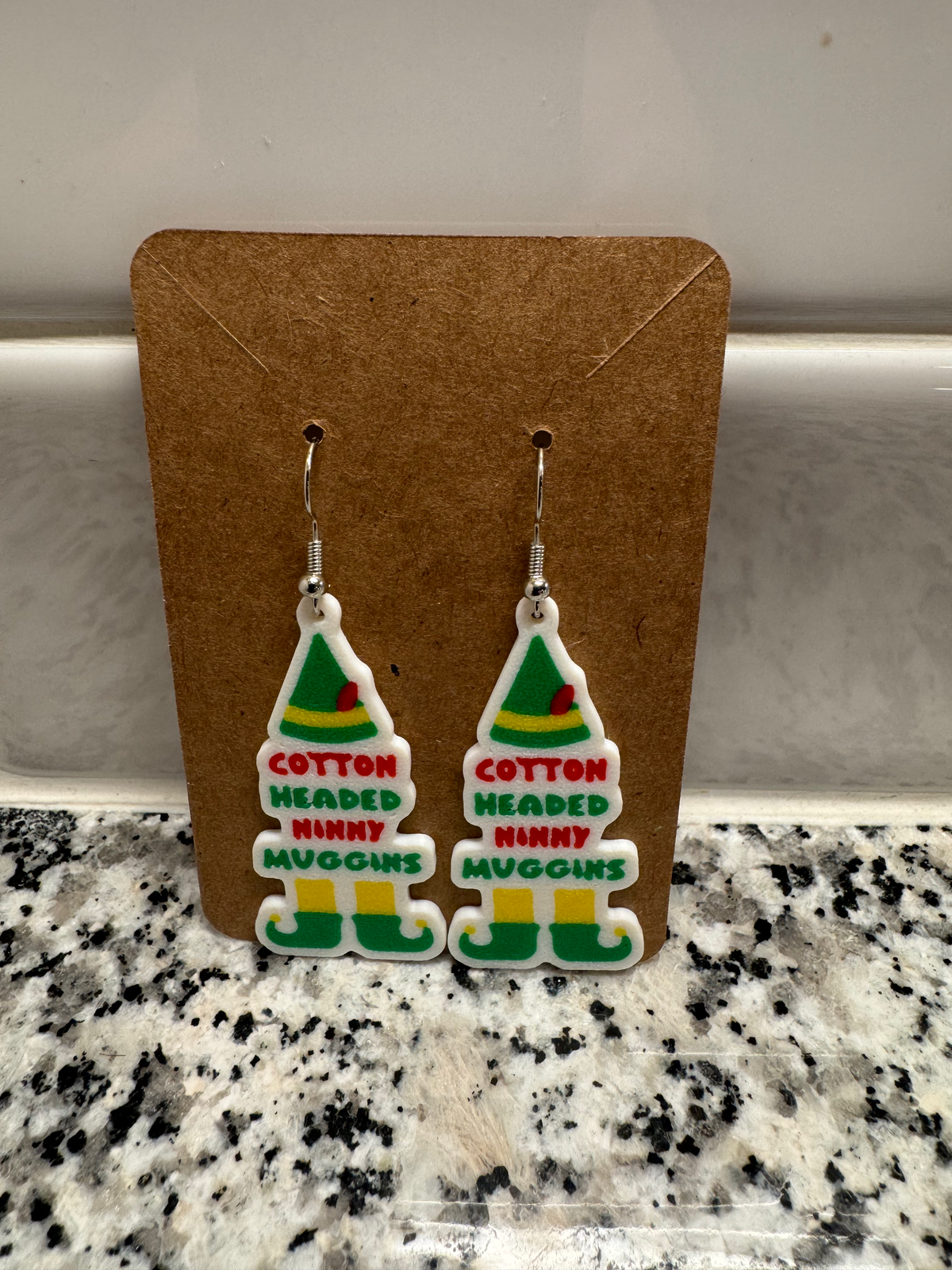 Elf Hat Dangle Earrings — a pair of flat layered dangle earrings with raised lettering, on silver hooks.