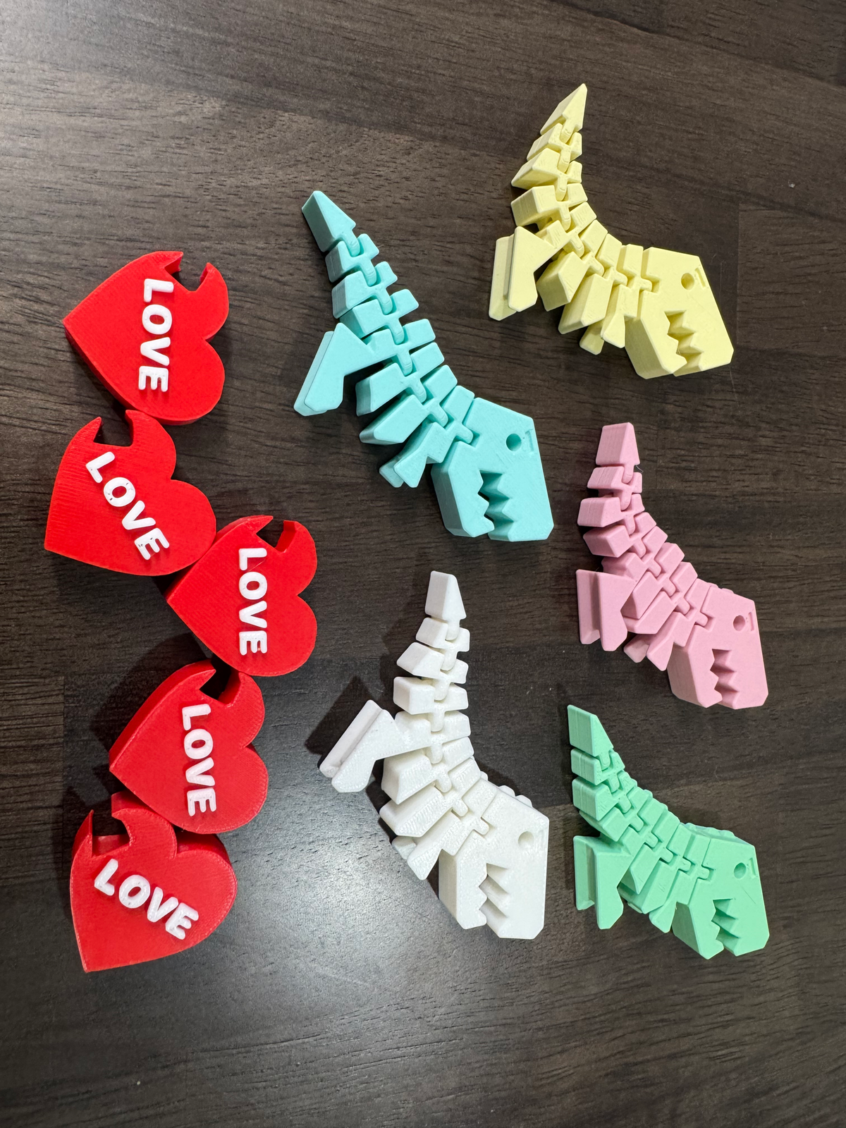 Flexi Dino Valentines — the dinosaurs and hearts laid out flat on dark wood, showing the jointed segments.