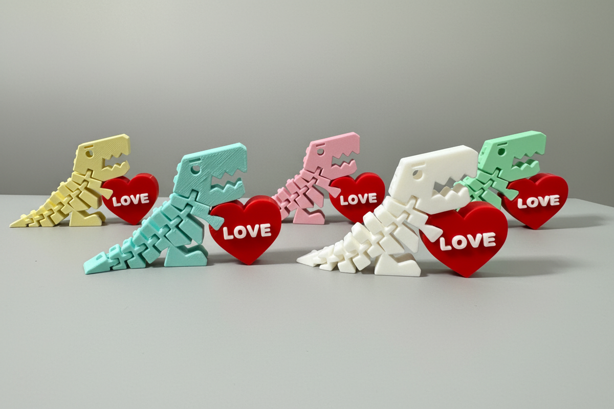Flexi Dino Valentines — five 3D-printed dinosaur toy figures in yellow, mint green, pink, white, and light green, each holding a red heart-shaped tag reading "LOVE," on a soft light-gray studio background.