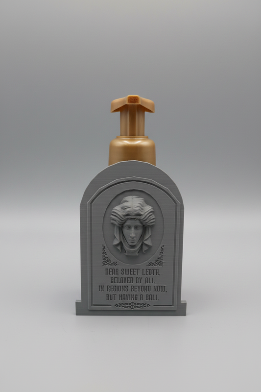 Fortune Teller Tombstone Soap Dispenser Holder — a grey tombstone-shaped holder with an engraved face panel, sized for a foaming soap bottle, on a soft light-gray studio background.