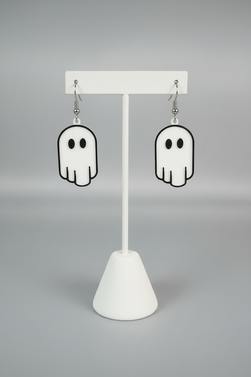 Ghost Earrings — a pair of white ghost-shaped dangle earrings with black outlines and silver hooks, on a soft light-gray studio background.