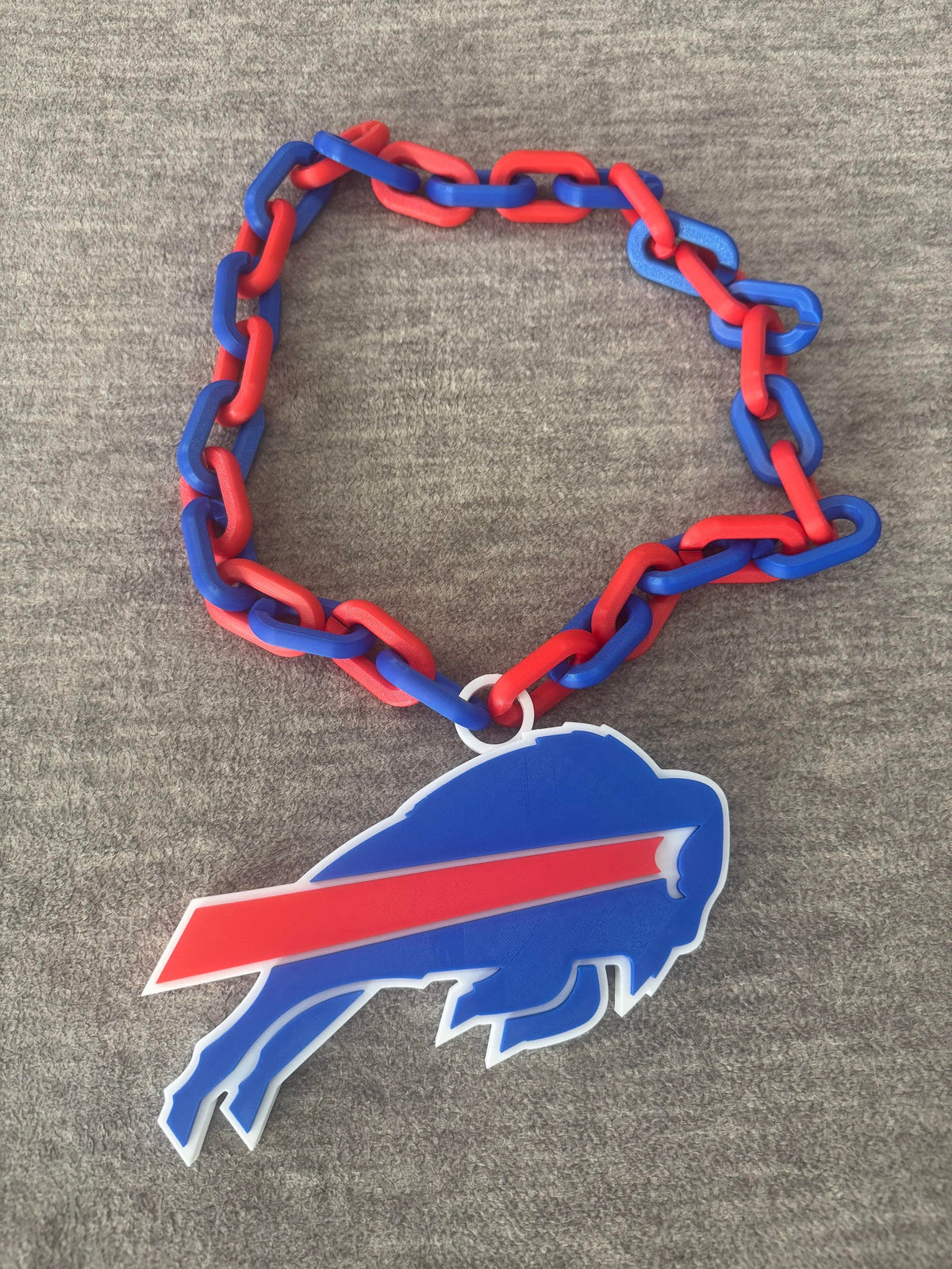 Giant Buffalo Football Necklace — a large flat pendant on a chunky red and blue interlocking chain, laid out on a grey seat.