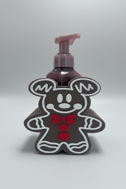 Gingerbread Mouse Soap Dispenser Holder — a brown gingerbread-themed pump bottle holder with a mouse-silhouette design, white outlines, and a red bow tie, holding a dark purple pump bottle, on a soft light-gray studio background.