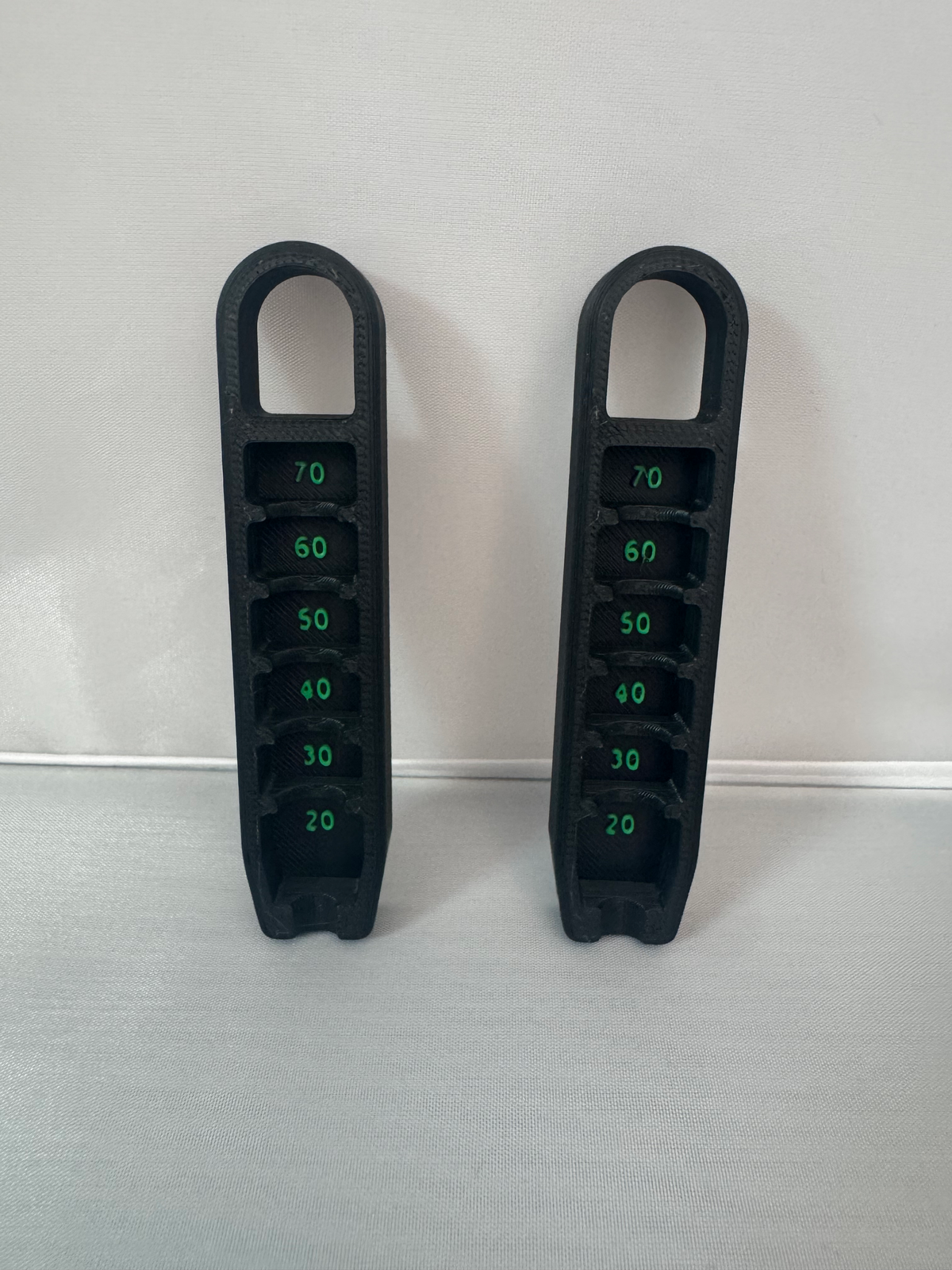 Golf Tee Height Gauge — two black gauges with stepped slots numbered 20 to 70 in green, shown side by side.