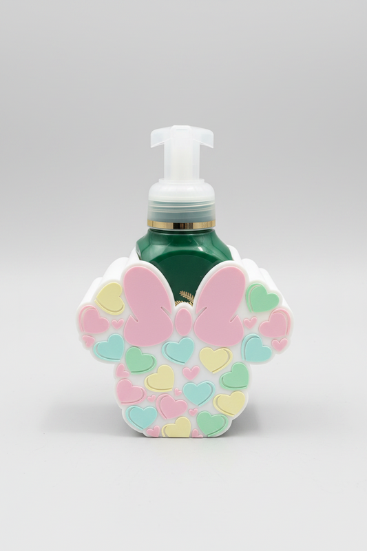 Heart Bow Soap Dispenser Holder — a green pump bottle of liquid soap housed in a decorative white character-head-shaped holder, decorated with pink, yellow, and mint green hearts, on a soft light-gray studio background.