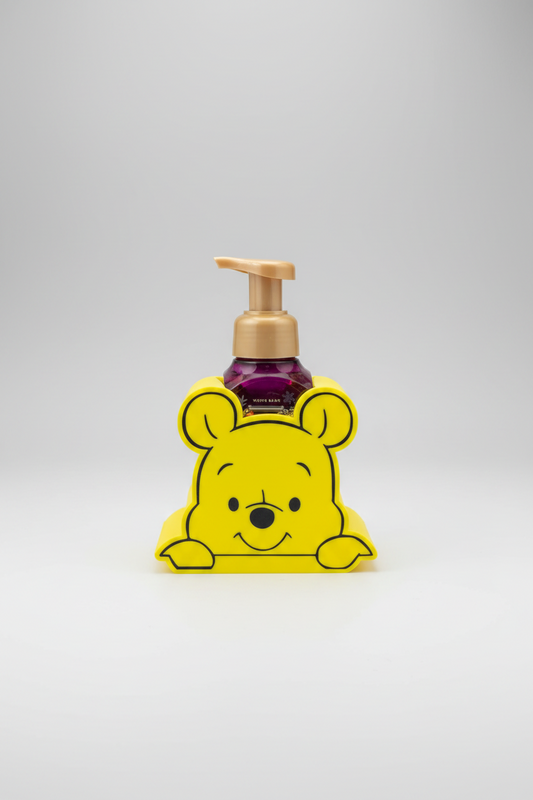 Honey Bear Soap Dispenser Holder — a yellow bear-shaped soap dispenser holder containing a purple pump bottle, on a soft light-gray studio background.