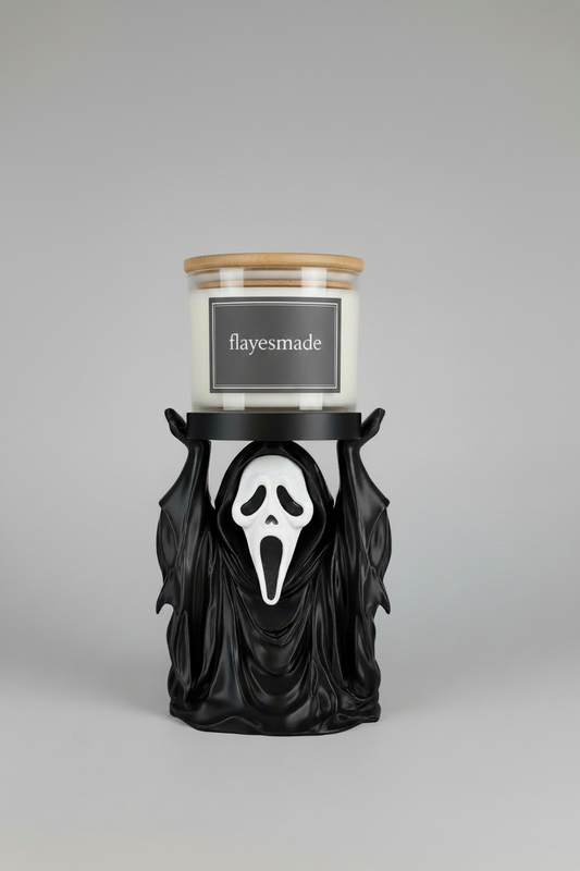 Hooded Ghost Candle Holder — a black draped figure with a pale mask and raised arms supporting a round tray, holding a jar candle, on a soft light-gray studio background.