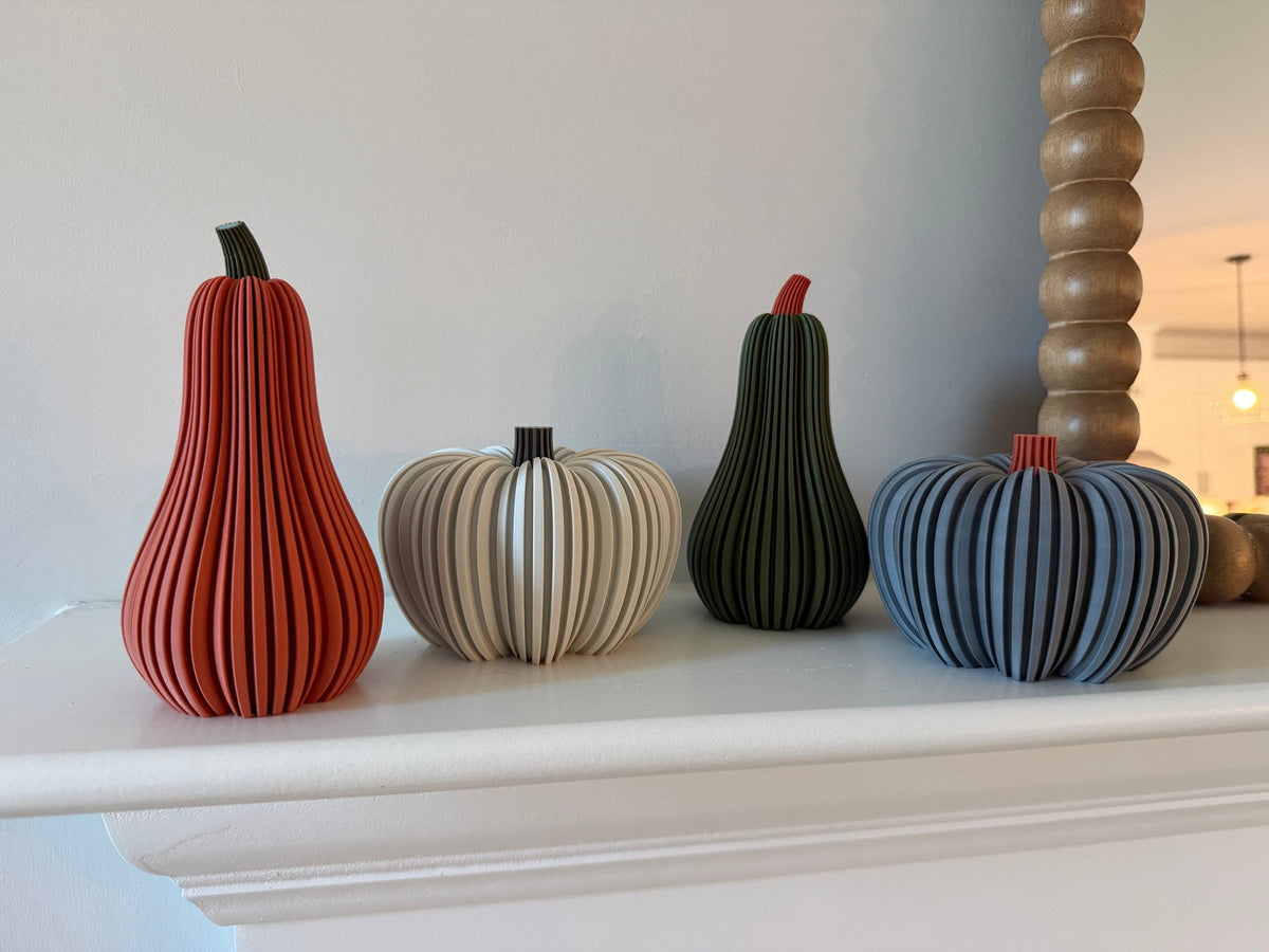 Modern Ribbed Pumpkin — four ribbed pumpkins and gourds in rust, cream, green and blue lined up on a white mantel.