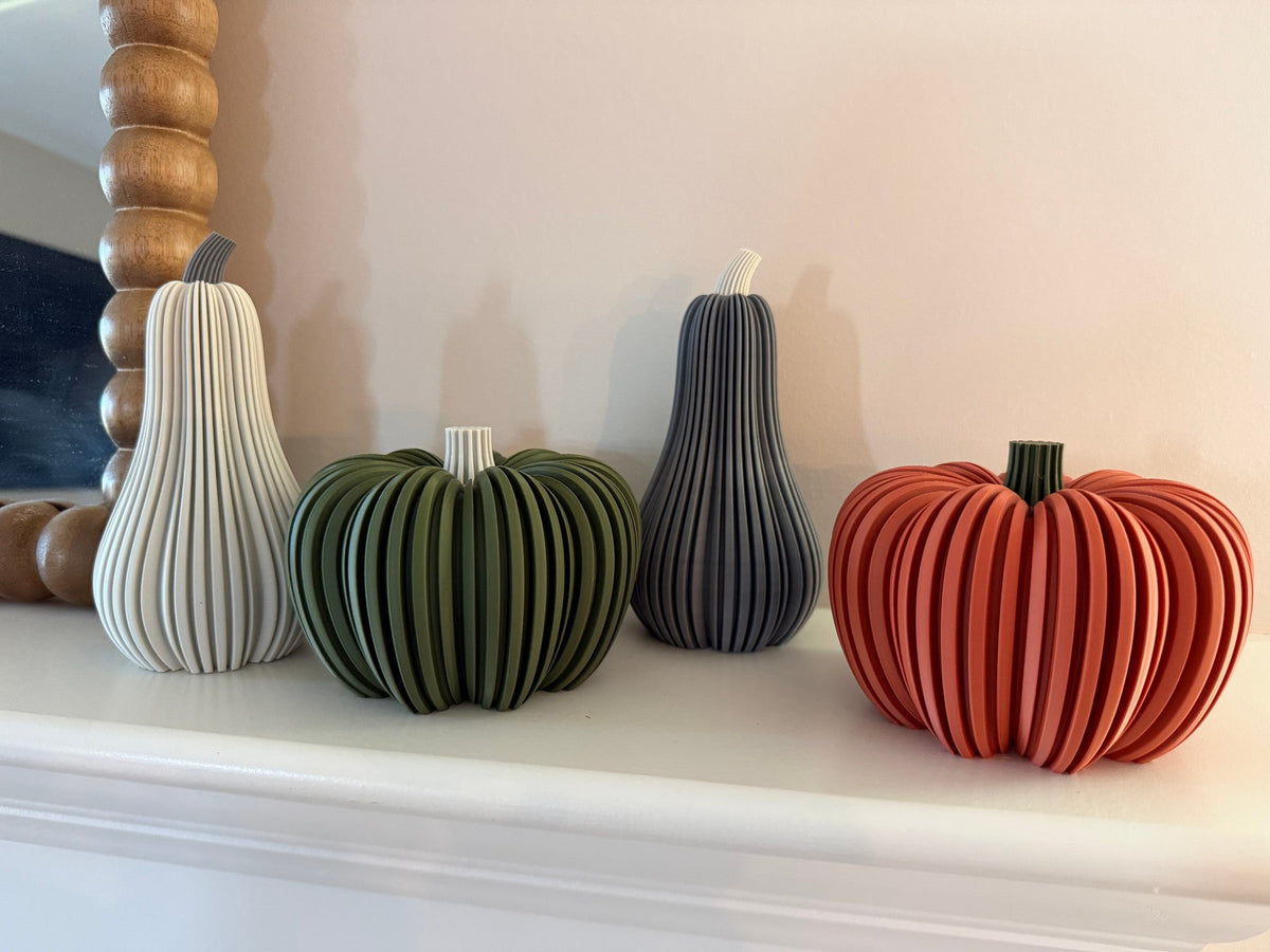 Modern Ribbed Pumpkin — ribbed pumpkins in white, green, charcoal and rust displayed on a white mantel beside a beaded mirror.