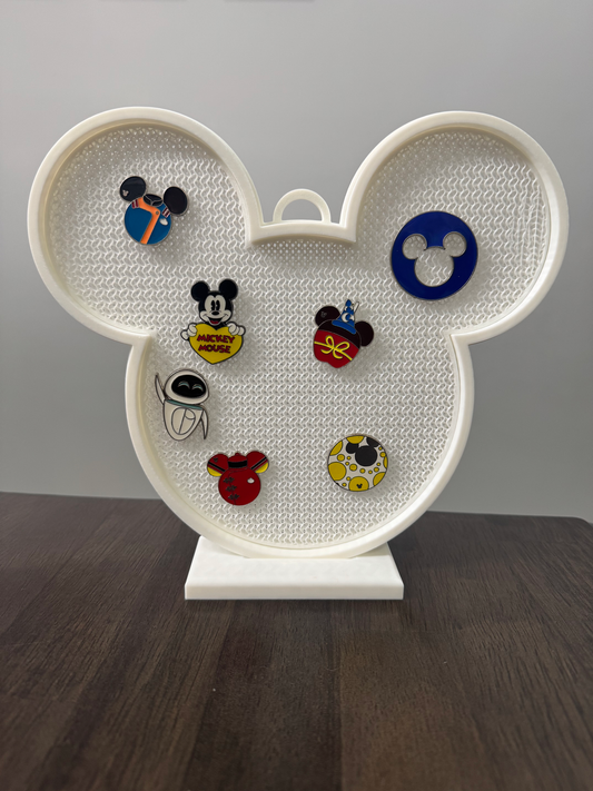 Mouse Head Pin Display Board — a white rounded display board with two ear shapes and a textured pin-backing surface on a stand, holding several enamel pins.