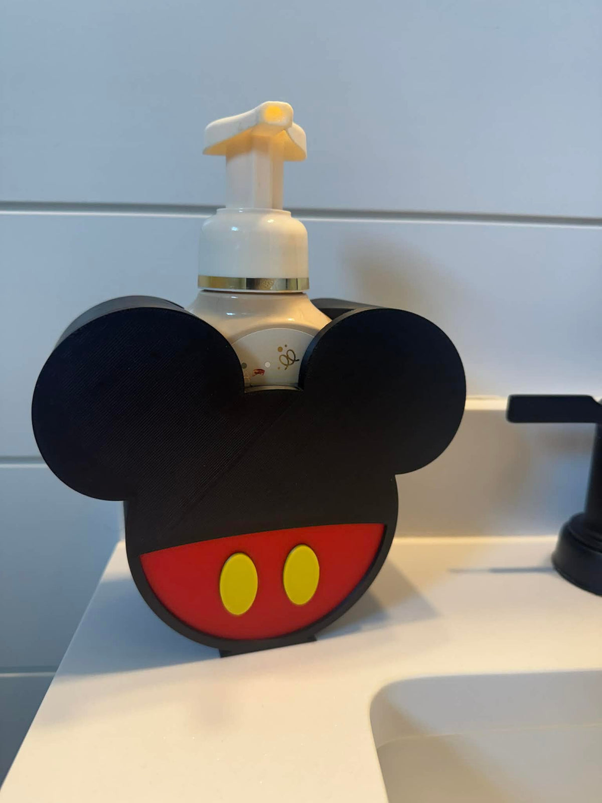 Mouse Head Soap Dispenser Holder — a rounded holder with two ear shapes and a red and yellow lower panel, holding a foaming soap bottle at a bathroom sink.