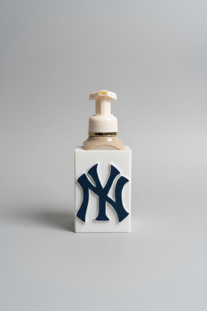 New York Soap Dispenser Holder — a white rectangular sleeve with a raised navy monogram, holding a foaming soap bottle with a cream pump, on a soft light-gray studio background.