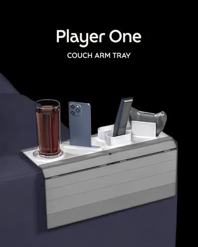 Player One Modular Sofa Side Table — a grey slatted couch arm tray holding a drink, a phone, a controller stand and a remote, draped over a sofa arm.