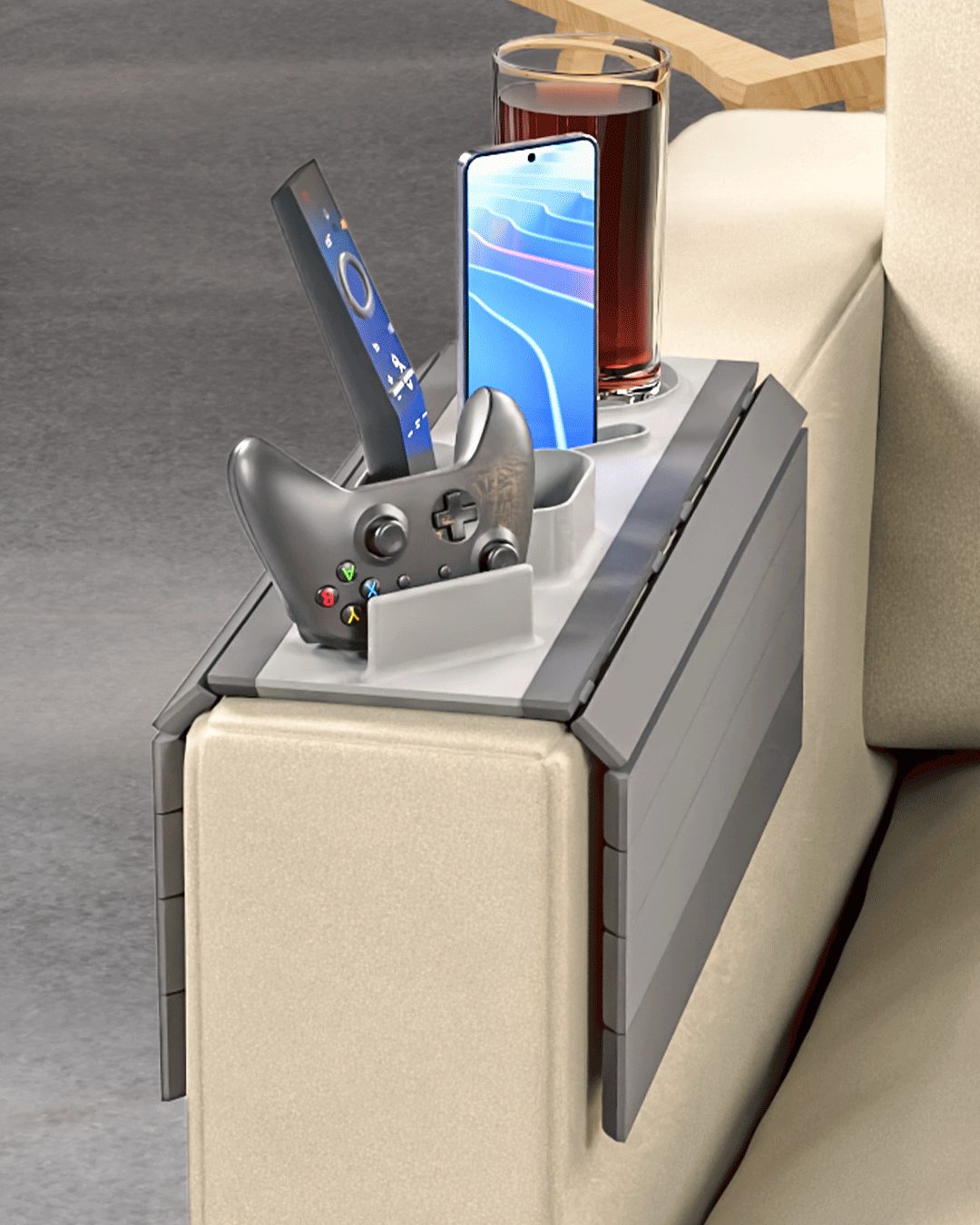 Player One Modular Sofa Side Table — the arm tray on a cream sofa arm with a game controller in its cradle, a phone upright, a remote and a drink in the cup holder.