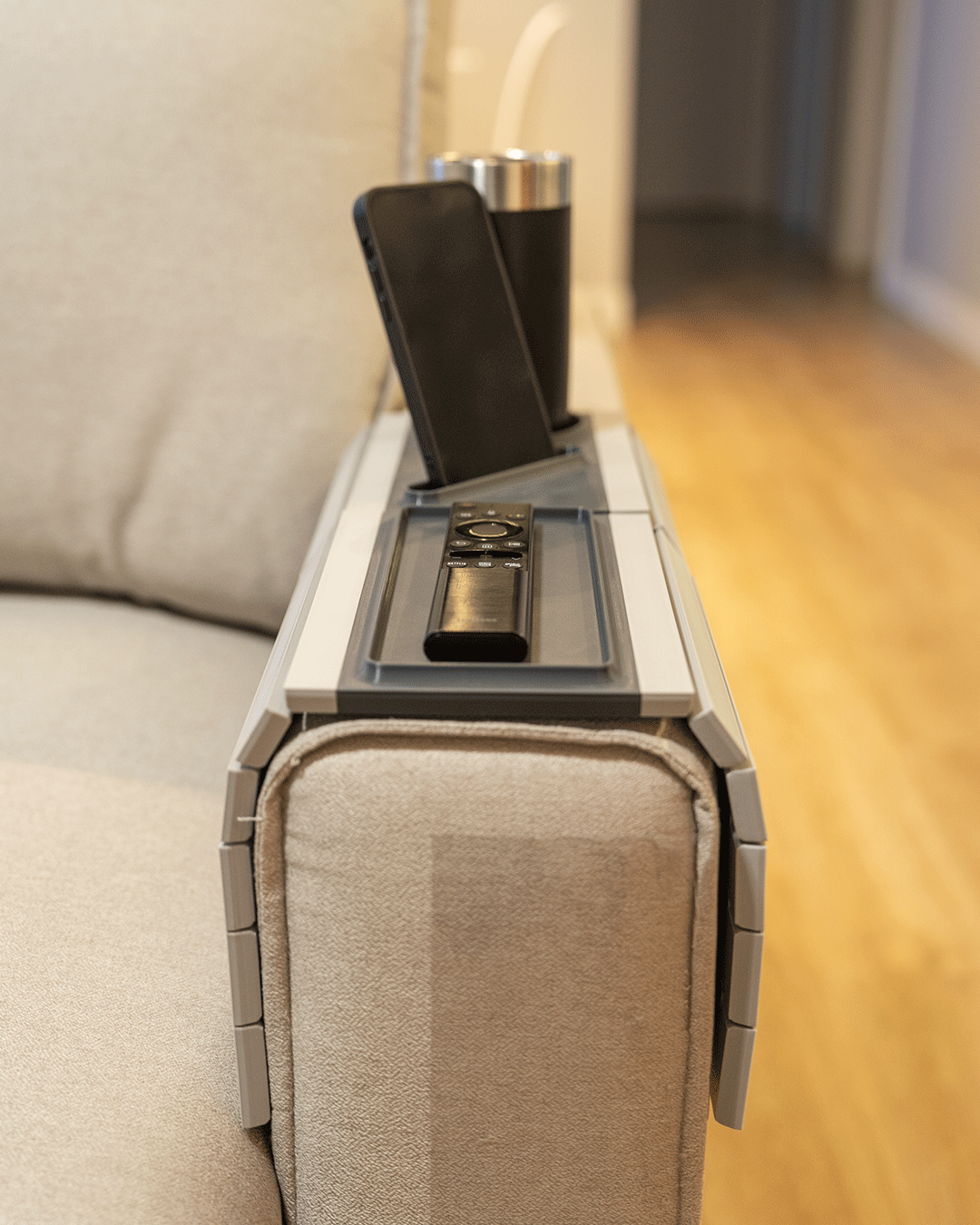 Quick Rest Modular Sofa Side Table — the slatted tray folded over a cream sofa arm holding a phone, a remote and a tumbler.
