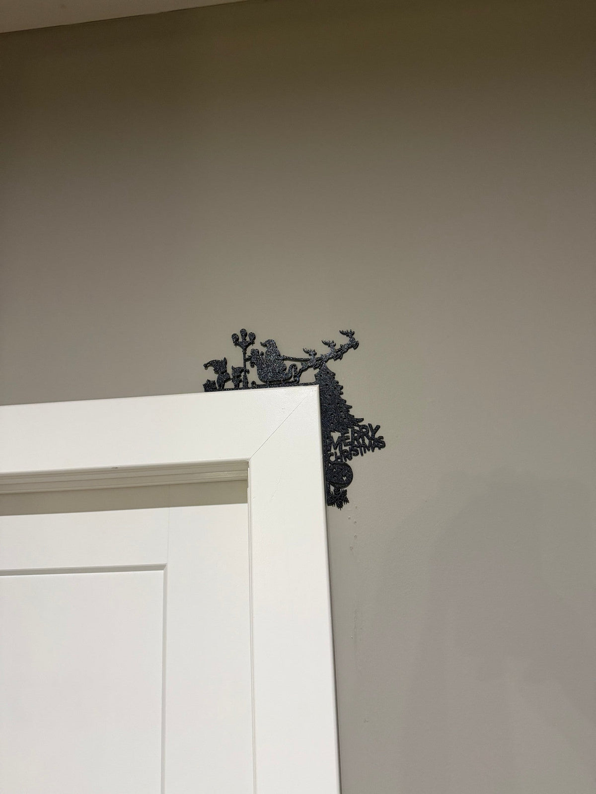 Reindeer Sleigh Corner Door Topper — a black silhouette of a reindeer and sleigh perched on the top corner of a white door frame.