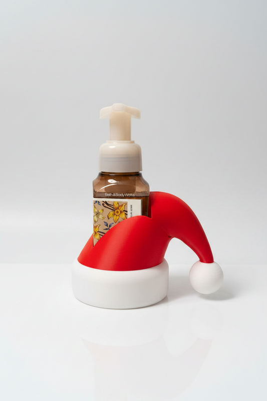 Santa Hat Soap Dispenser Holder — a frosted glass pump bottle with brown liquid in a holiday Santa hat-shaped holder, on a soft light-gray studio background.
