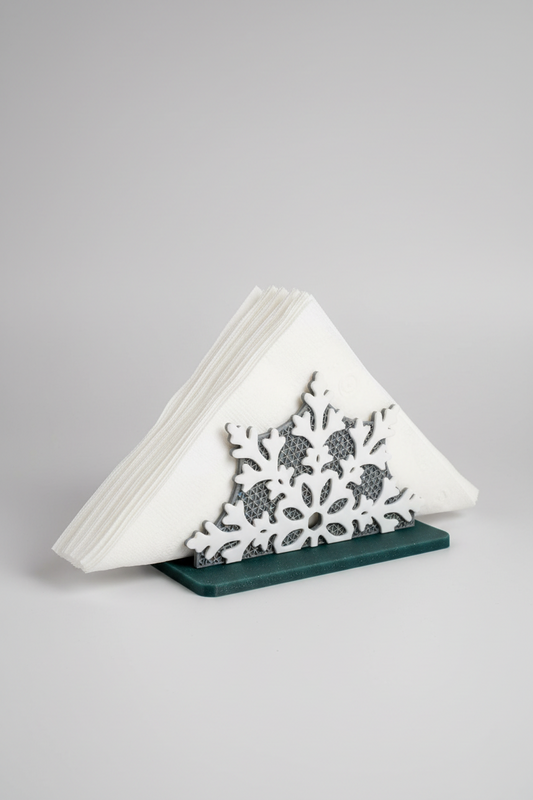 Snowflake Napkin Holder — a white snowflake-shaped napkin holder with a dark green base, holding a stack of white paper napkins, on a soft light-gray studio background.