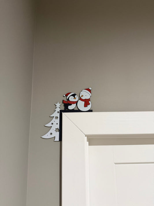 Snowman Penguin Tree Corner Door Topper — a white tree with a snowman and a penguin in red scarves, perched on the top corner of a white door frame.