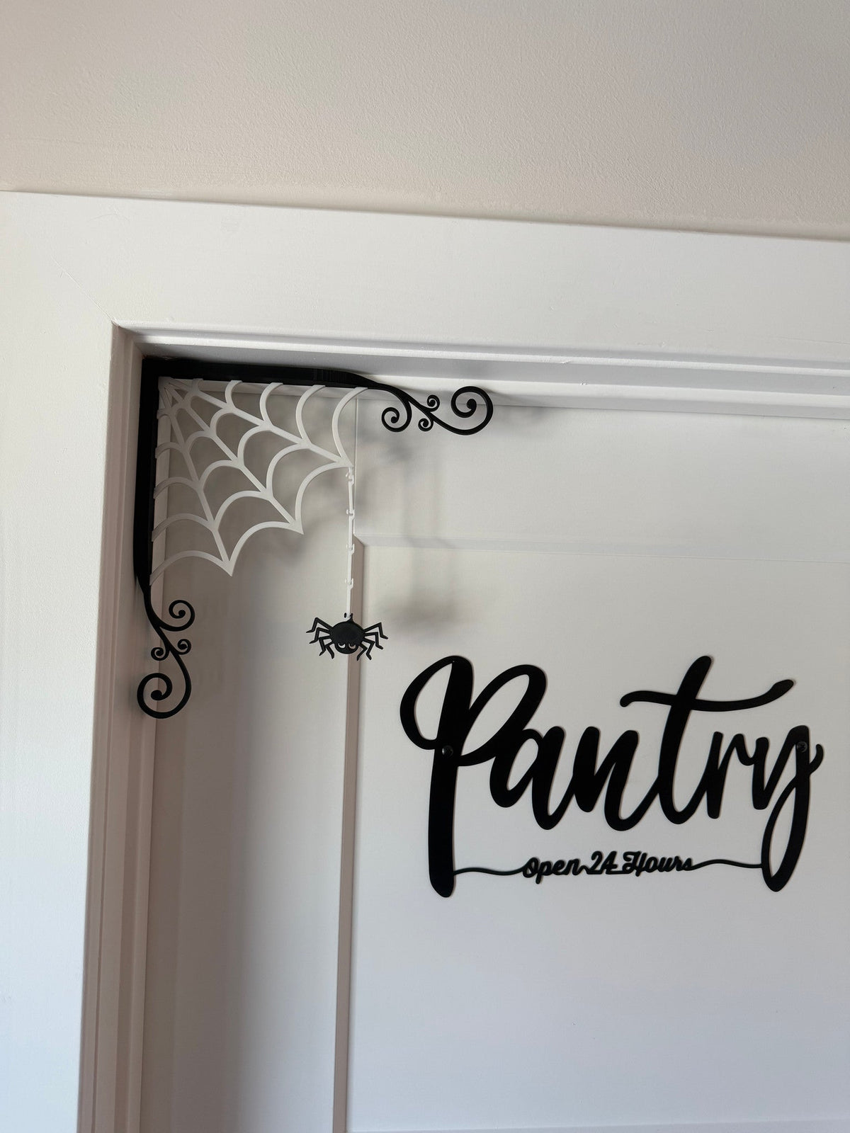 Spiderweb Corner Door Topper — a white spiderweb with a black scrollwork border and a dangling spider, fitted into the top corner of a doorway.