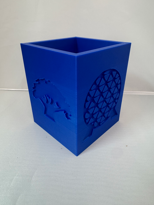 Theme Park Multi-Purpose Holder — a blue open-topped square holder with raised silhouette panels on each side, on a white surface.