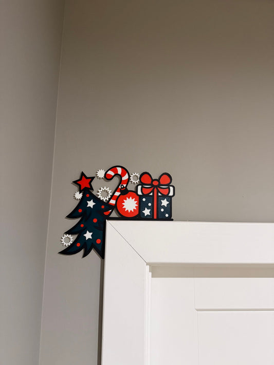 Tree Gift Candy Cane Corner Door Topper — a navy tree, candy cane and wrapped gift in red, white and blue, perched on the top corner of a white door frame.